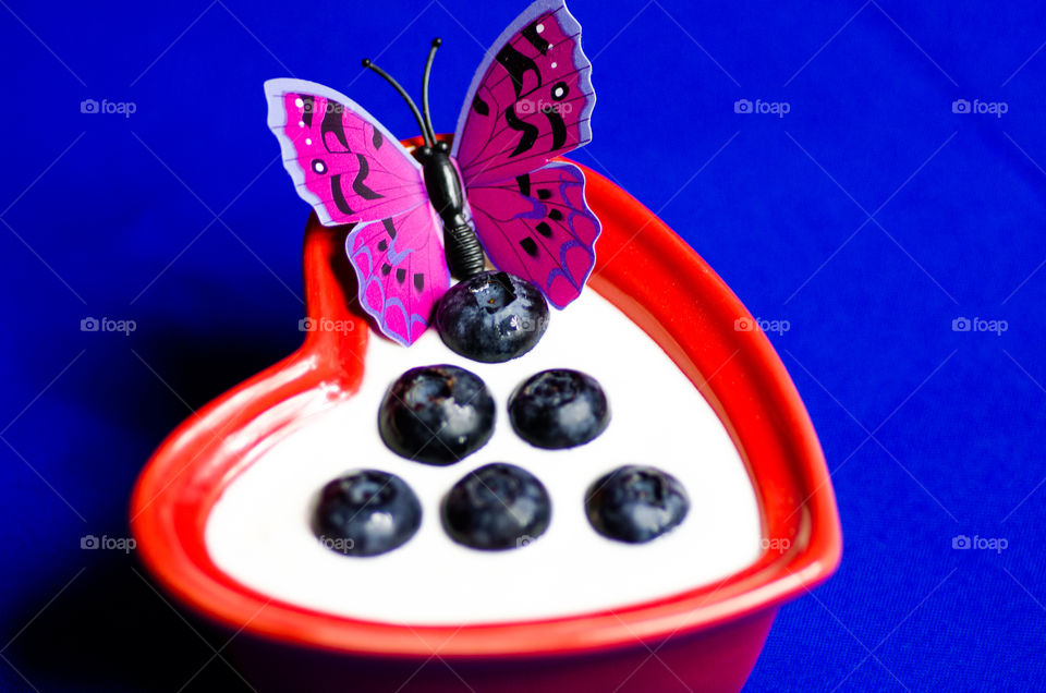 Blueberries in a heart shaped bowl with yoghurt and butterfly