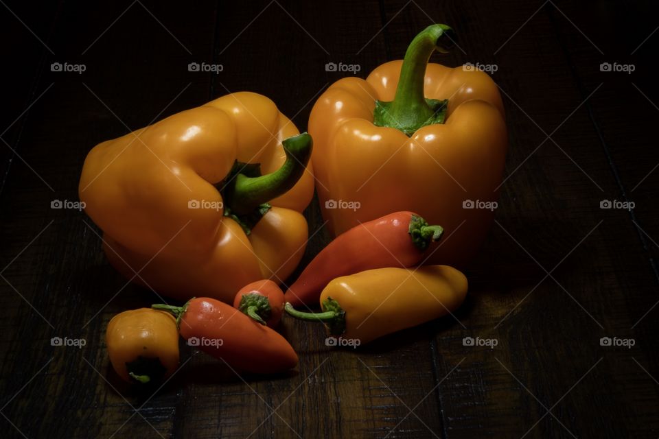 A still life of red and yellow bell peppers and sweet peppers with a dark background. 
