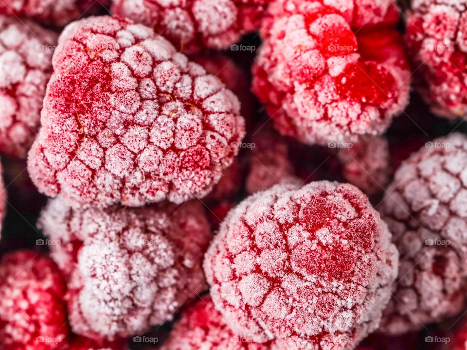 Beautiful background of frozen raspberries with a white snow pattern, flat lay close-up.