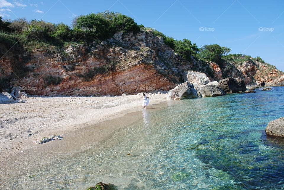 A woman in white on the beach under the cliff