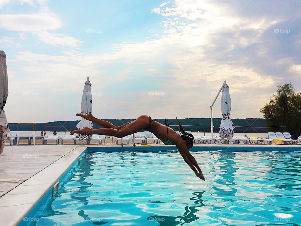 Young woman jumping into the blue swimming pool outdoors 