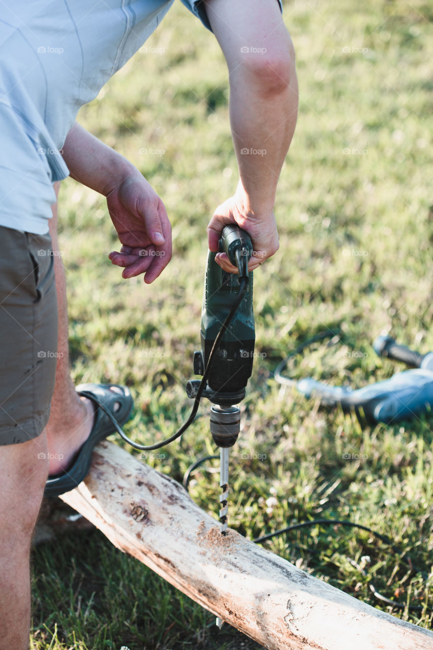 Man drilling hole in timber while working in garden. Real people, authentic situations