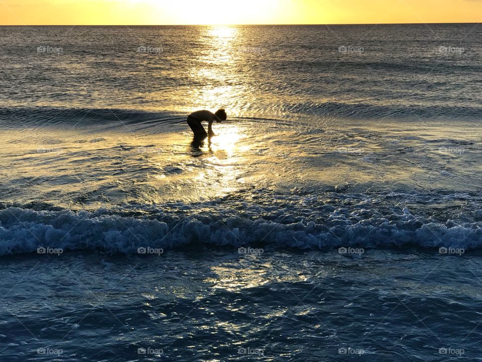 Small boy in the ocean surrounded by the light of a golden sunset.