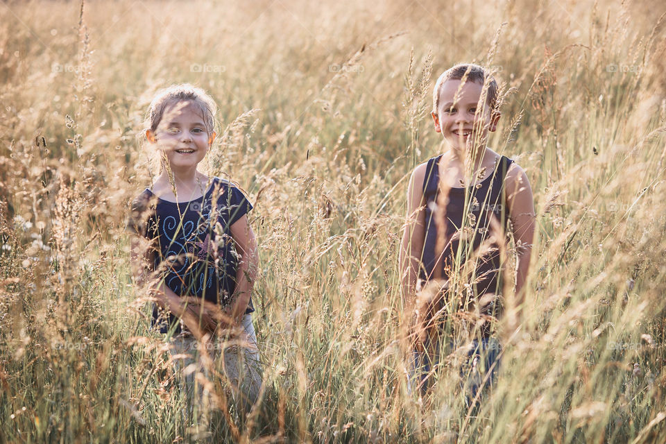 Little happy smiling kids playing in a tall grass in the countryside. Candid people, real moments, authentic situations