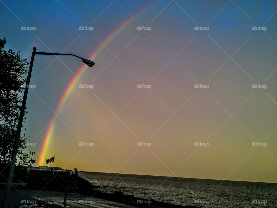 Rainbow across the sky shooting all the shades of red blue orange. Sky and the ocean greet the rainbow