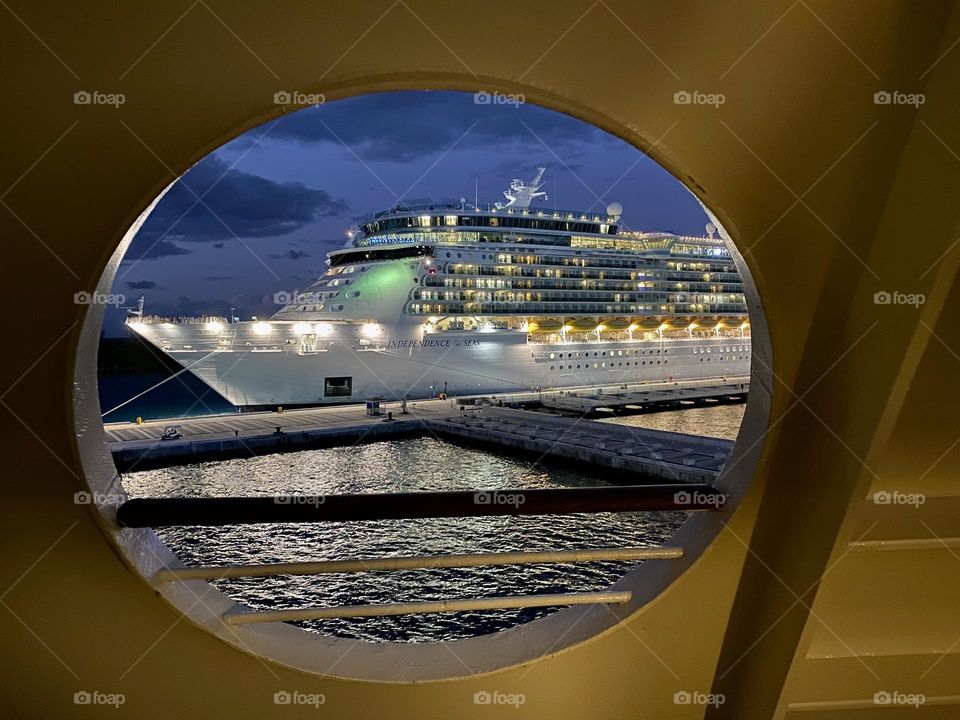 Looking through a round window towards a cruise ship at night