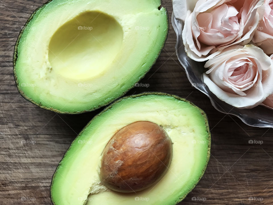 Overheard view of Halves of green ripe avocado and pastel roses on wooden background 