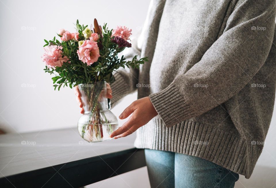 Bouquet of different flowers in vase in woman hands on table at home 