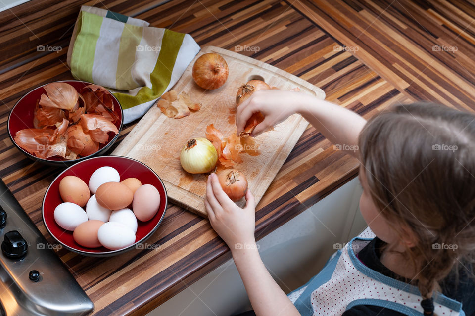 Little girl peeling off onions skins to use it as a natural dye in process of colouring Easter eggs.