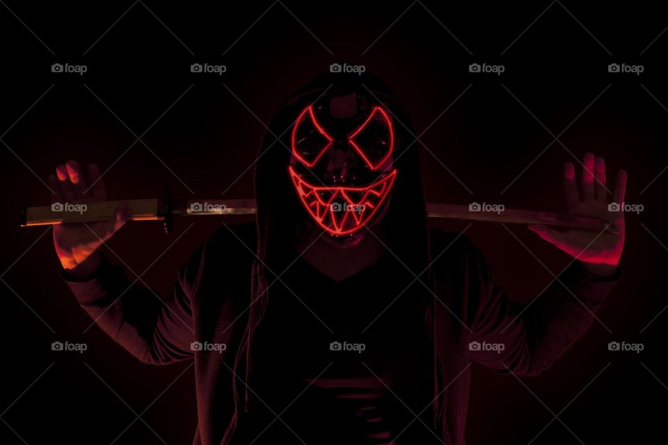 Man armed with a katana and wearing a scary glowing mask and a hoodie