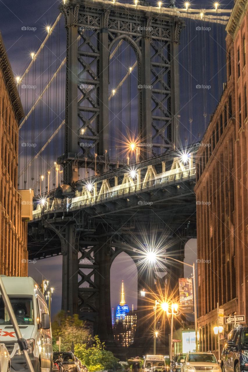 The Empire State Building framed within the legs of the Manhattan bridge. Blue and gold Notre Dame night. 