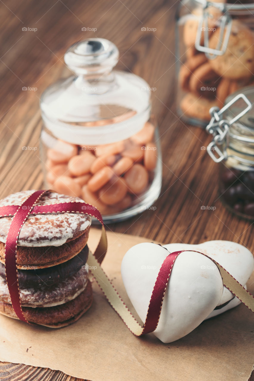 Gingerbread cookies, candies, cakes, sweets in jars on wooden table. Portrait orientation