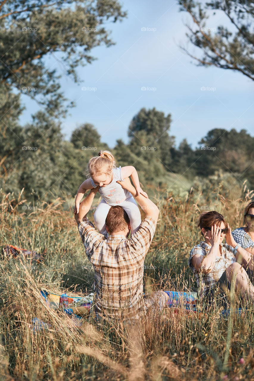 Family spending time together on a meadow, close to nature. Parents and children sitting and playing on a blanket on grass. Candid people, real moments, authentic situations