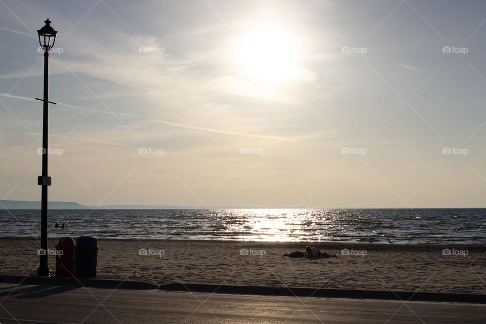 People lying on a sandy beach at sunset with a slightly wavy lake in the background