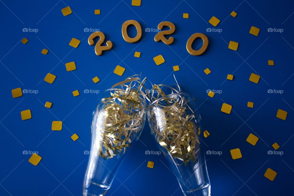 Conceptual flat lay of a champagne toast with glittering gold confetti and the numbers ‘2020’ in gold on a classic blue background - landscape format