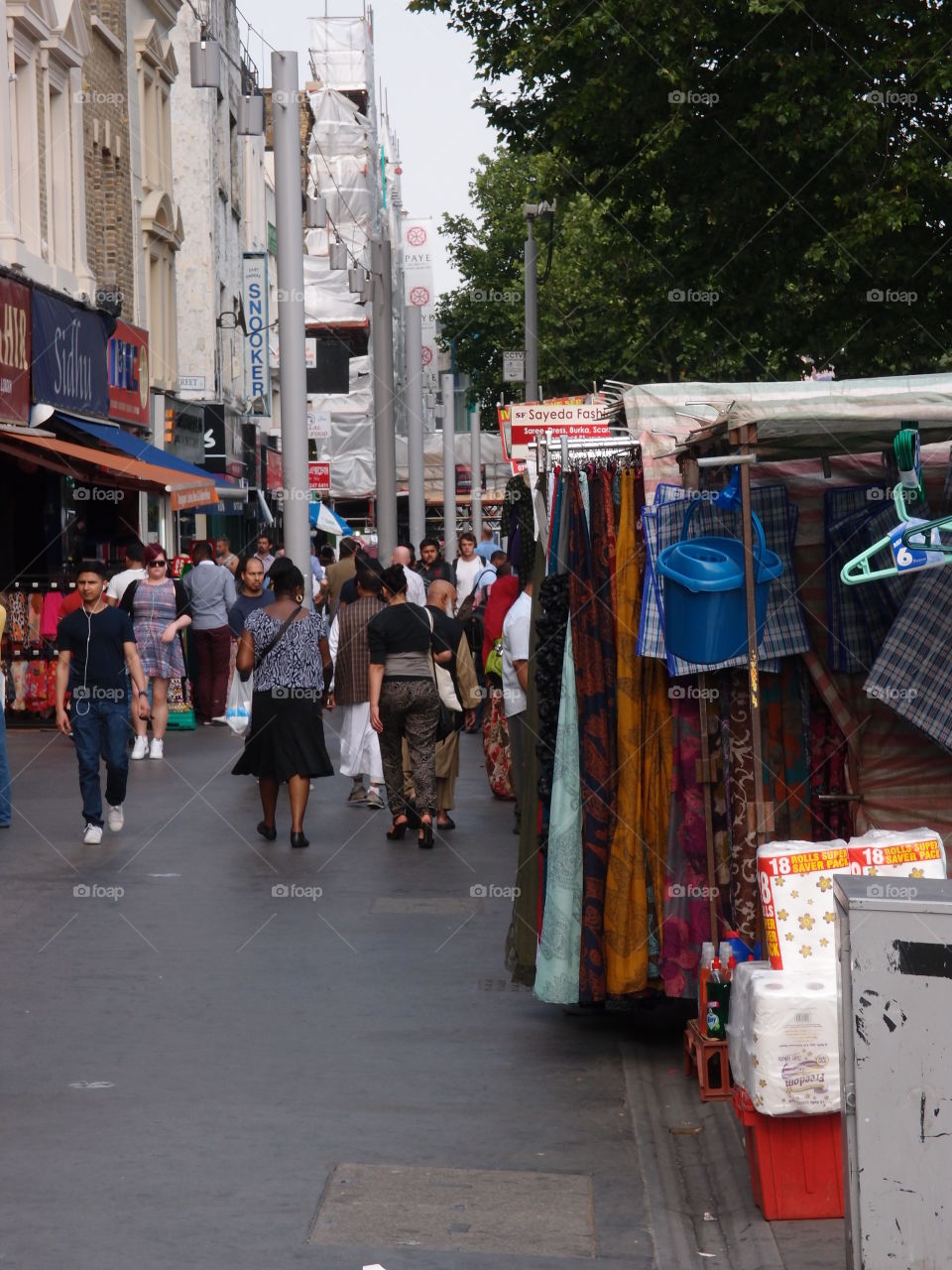 People walking on a sidewalk through an outdoor market in London on a summer day. 
