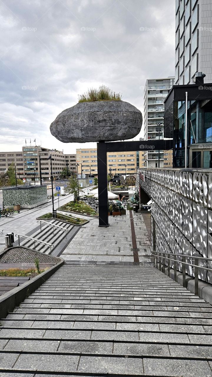 A gray rainy day in Finland in Helsinki Pasila. Behind you can see old buildings and in front on the right is the new shopping center tripla and its special stone statue