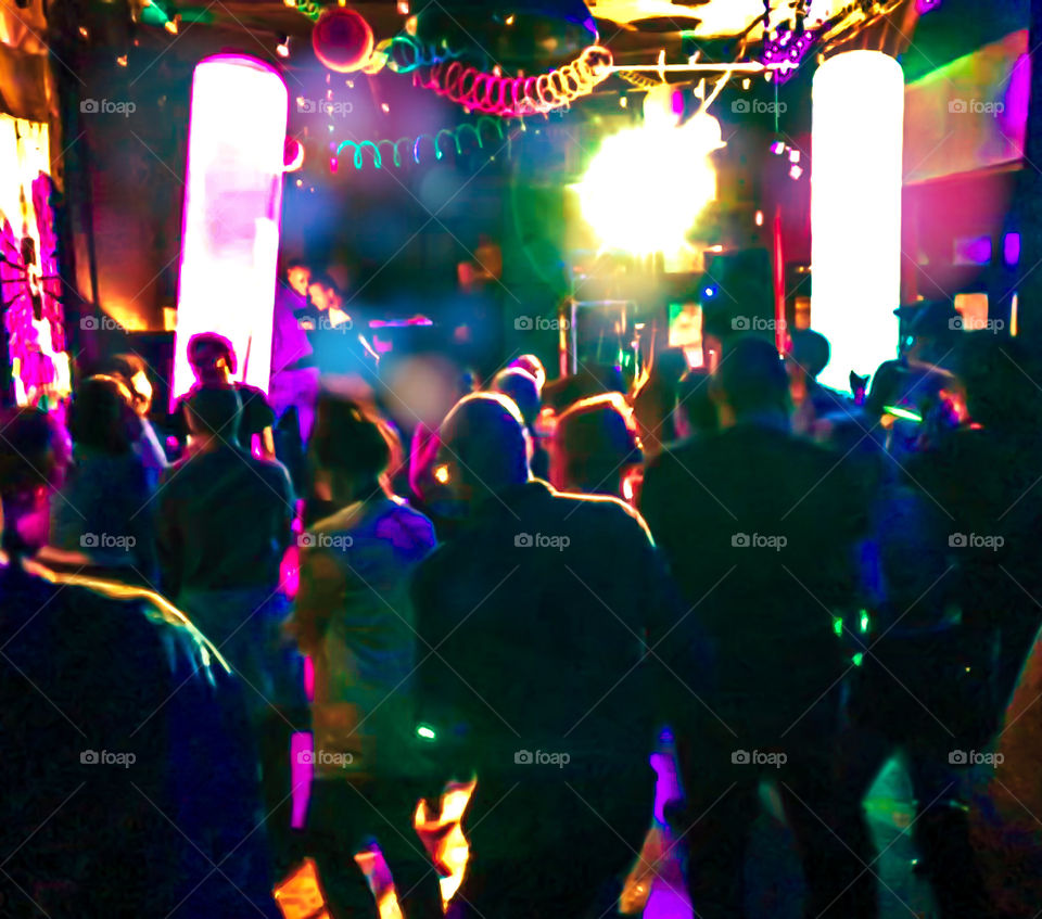 People dancing in a club, they are mostly silhouetted against the brightly coloured decor and lights, a DJ can be seen at the far end