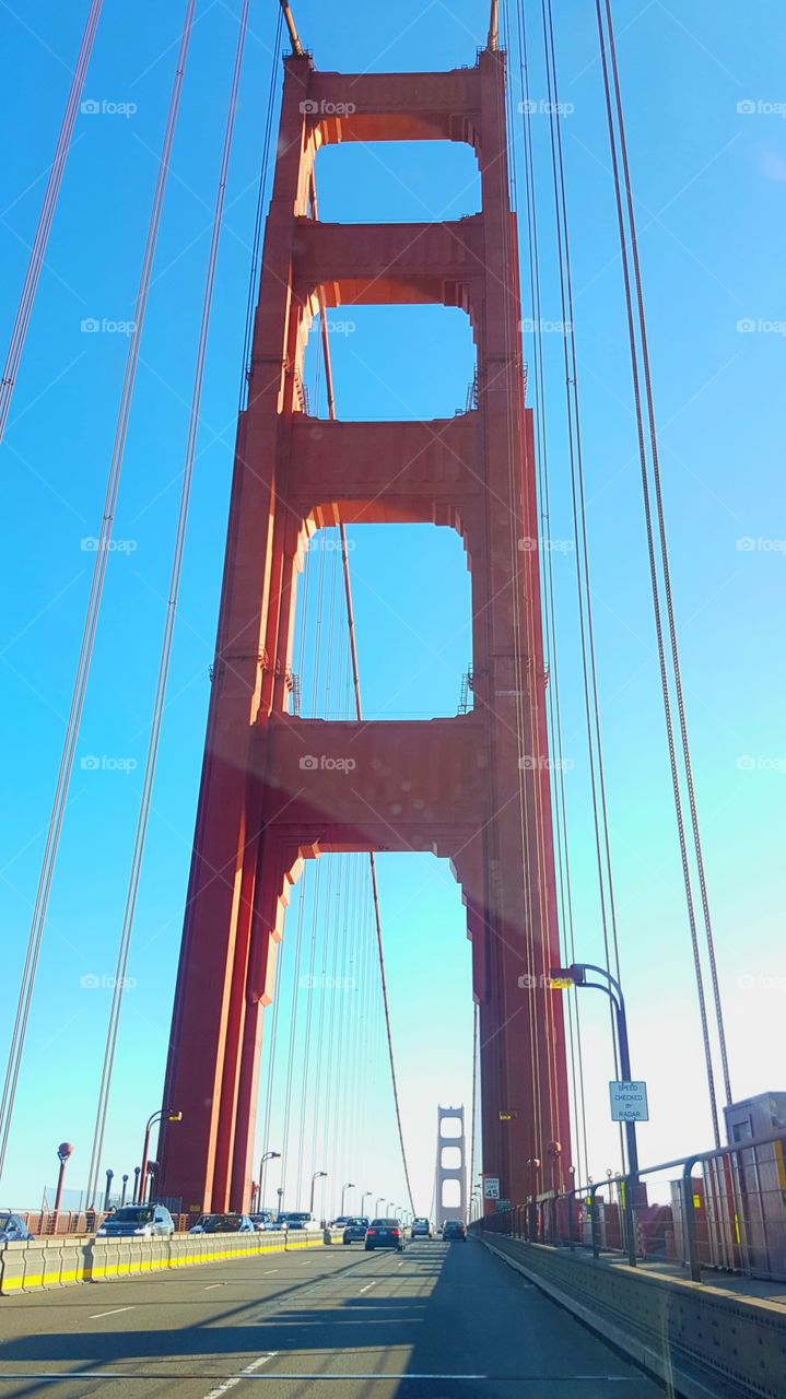 view from back window in Uber car ride, of the red colored Golden Gate Bridge in San Francisco, America, on happy sunny day with blue sky