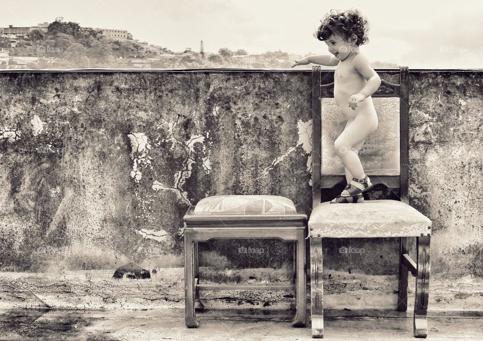 Little girl standing on chair behind wall