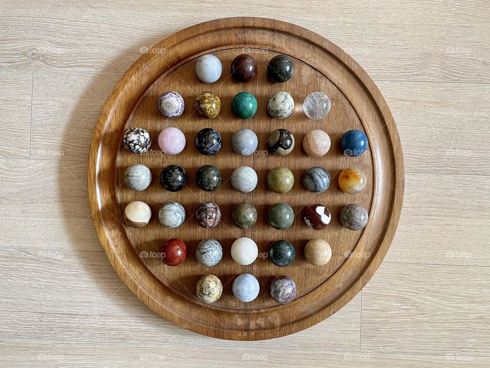 Multicolored polished crystal spheres - pink quartz, calcite, onyx, opal, brecciated jasper - various semiprecious stone balls for meditation on wooden tray. Top view.