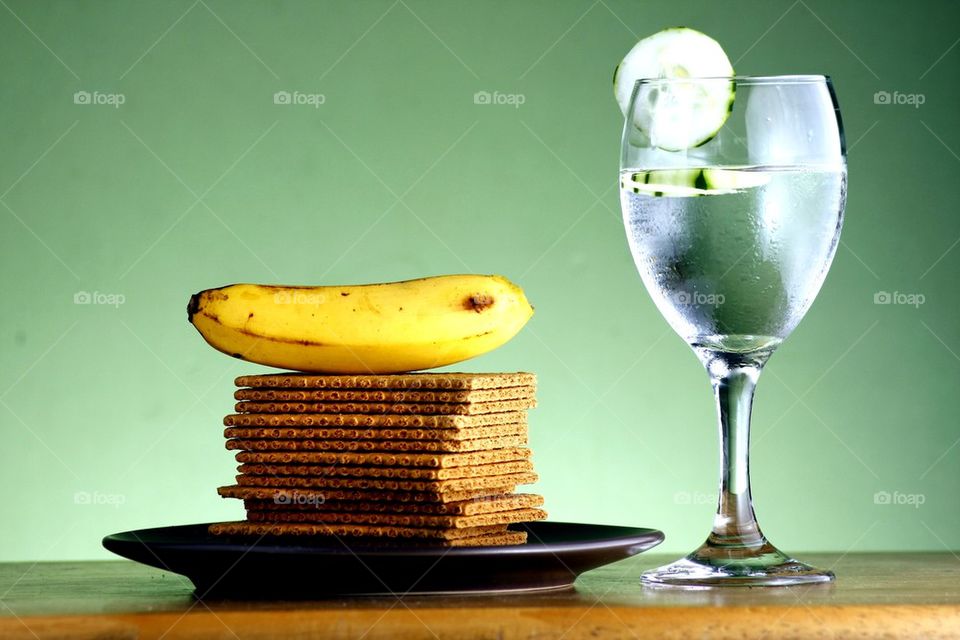 stack or pile of soda crackers, a banana and a goblet of water with cucumber slices