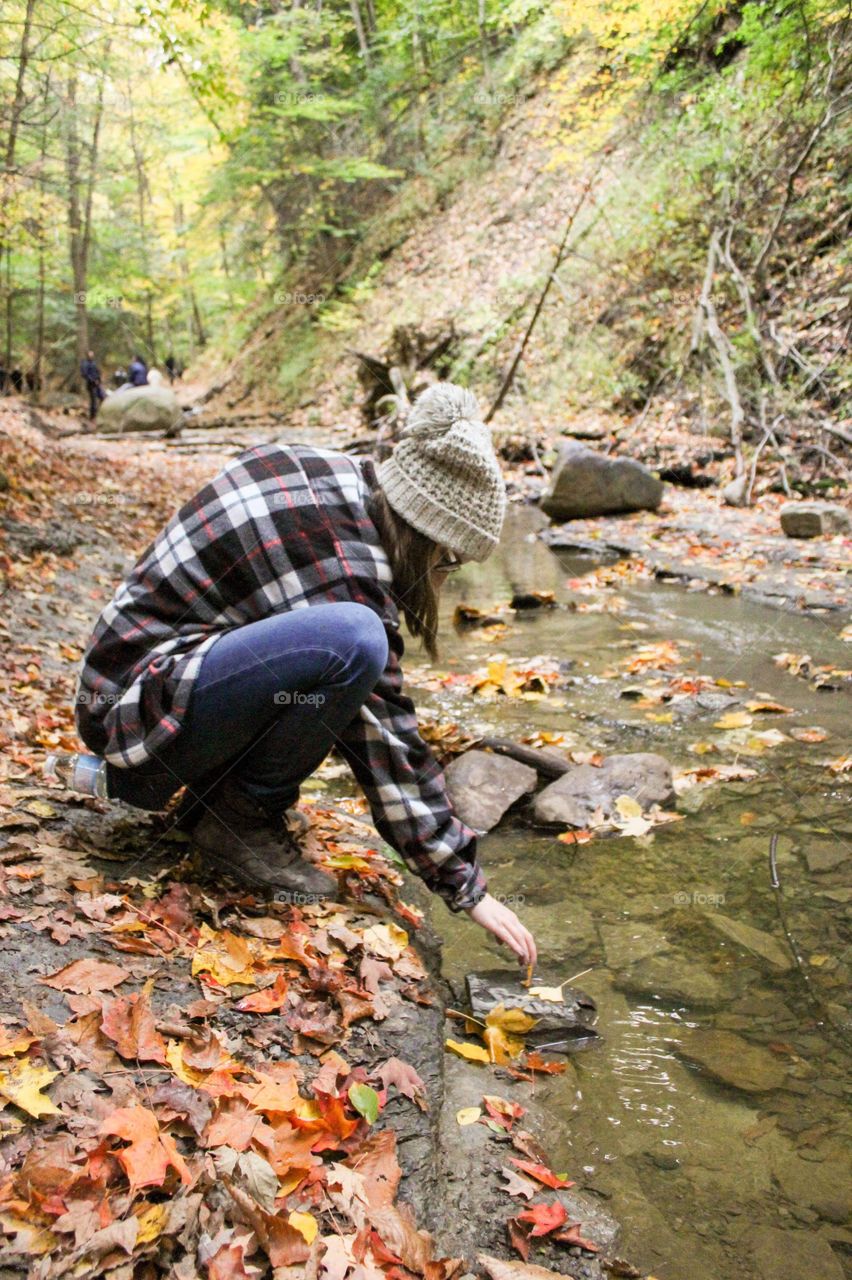 Young woman exploring a creek in the woods in the fall