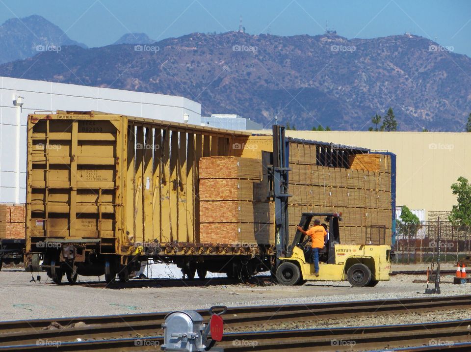 A forklift works to transfer lumber from two railcars to waiting trucks 