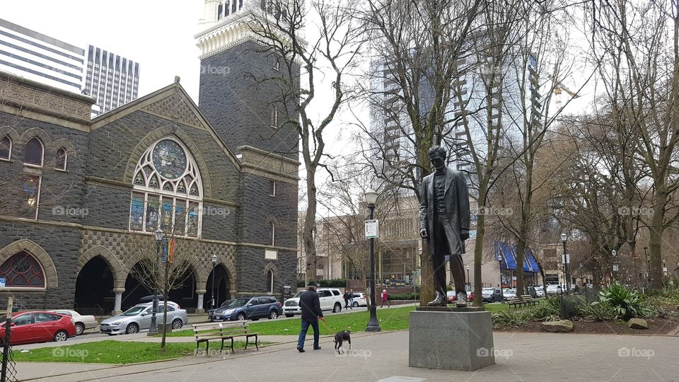 a church, buildings, man walking dog and statue in an American city