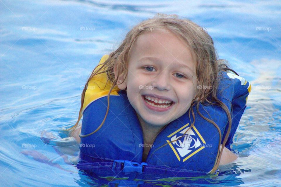 Pretty little girl happily swimming in the pool. 