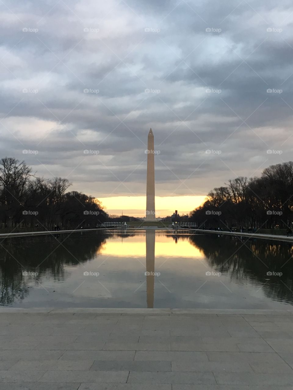 Sunset over the reflecting pool and behind the Washington monument of Washington DC. The overcast skies part slightly to let the last light of the day through