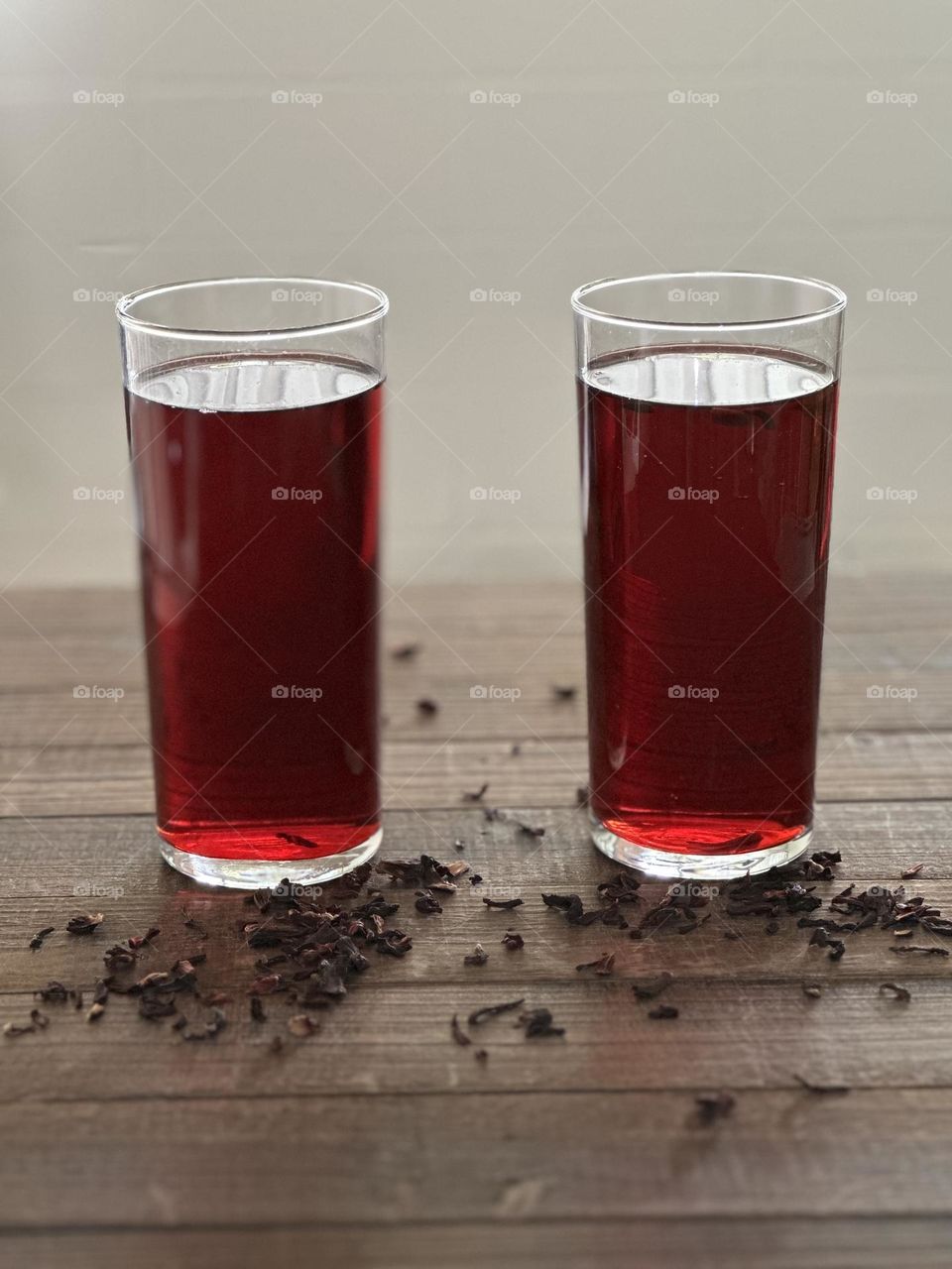 Two clear glasses of hibiscus tea with loose leaves on brown wood table