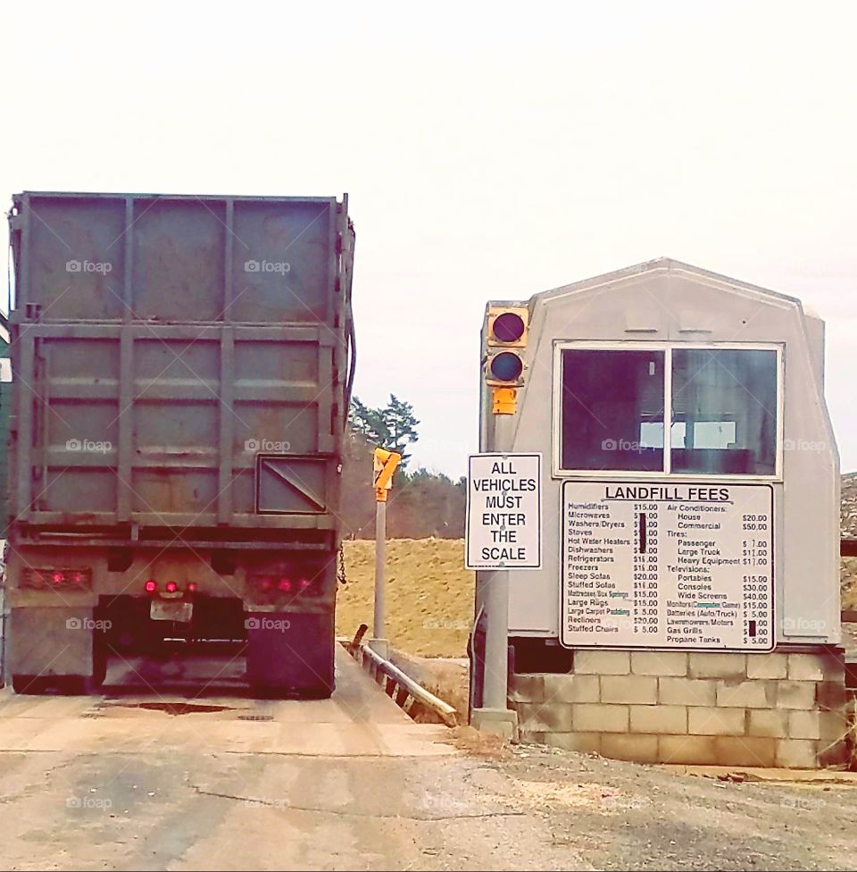 Landfill Entrance where fees are paid to dump & recycle. Building checks for stickers & money collection, dump truck stopped in front.