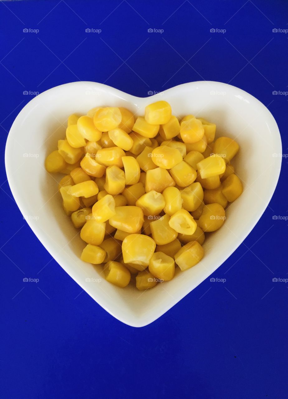 Beautiful bold yellow sweet corn. Bright yellow sweet corn in a heart shaped dish. Healthy food for a healthy heart. Flat lay style. Bold colours.