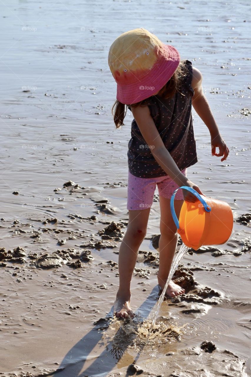 Girl playing on the beach pouring water from the bucket 