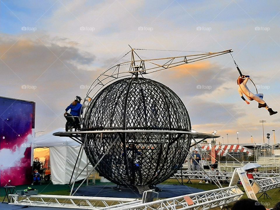 Daredevil and acrobat riding together around the metallic globe into the air.