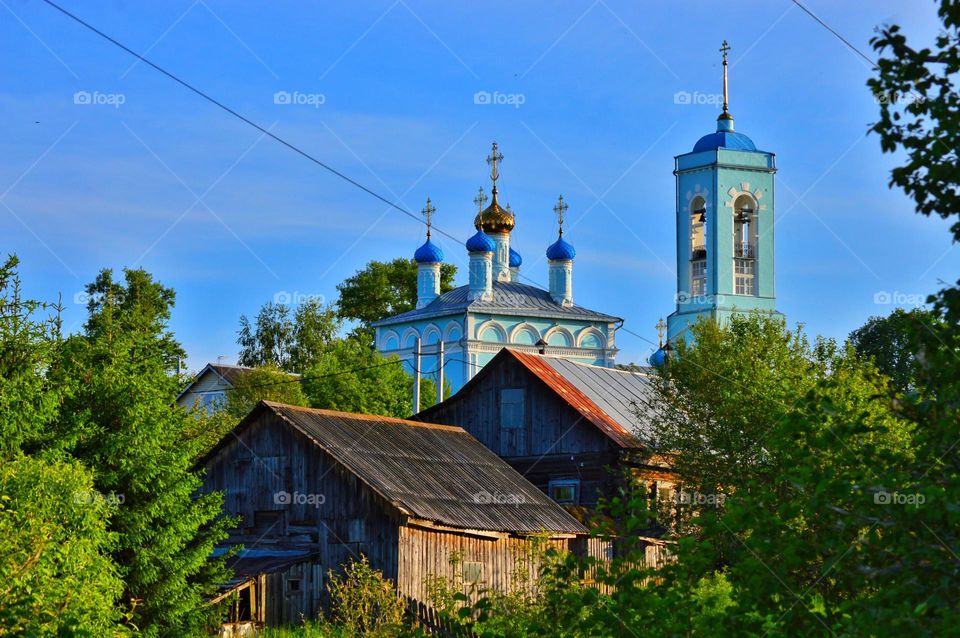 the photo shows old wooden residential buildings and in the background a blue village church. the harsh color of the Russian village