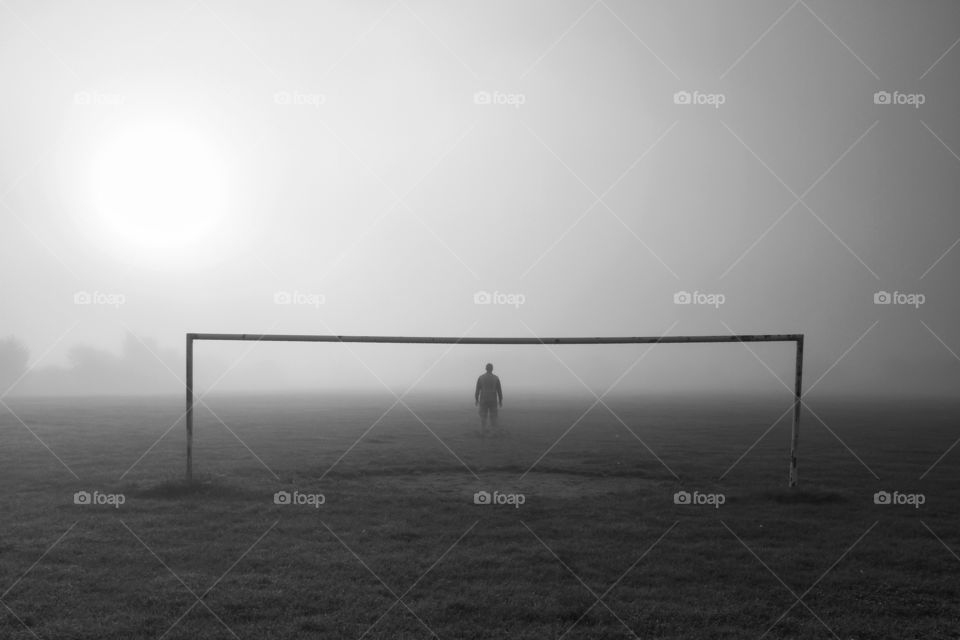 Goal keeper standing against goal post in foggy weather