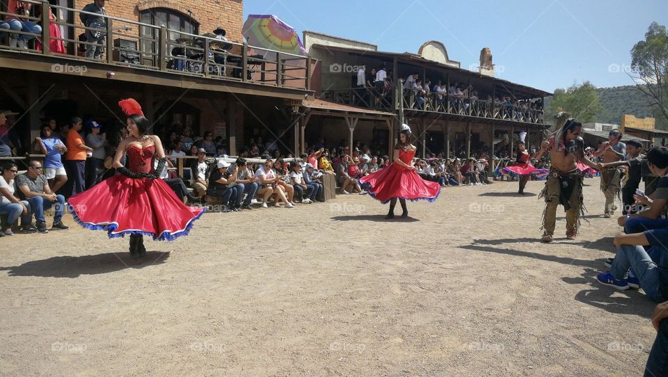 Women dressed with red skirts, dancing on rustic street.