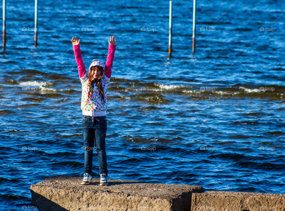 Excited girl standing on rock near sea