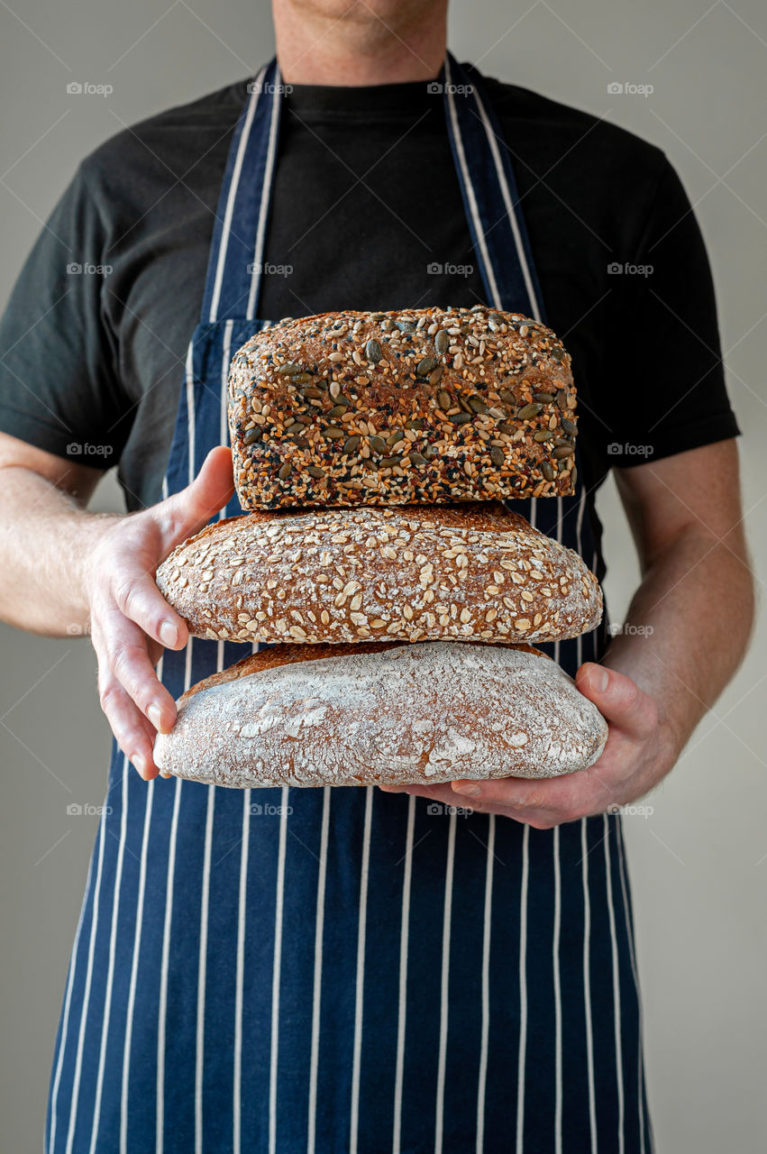 Close-up at bakers hands holding a selection of three organic loafs of sourdough bread in front of him.