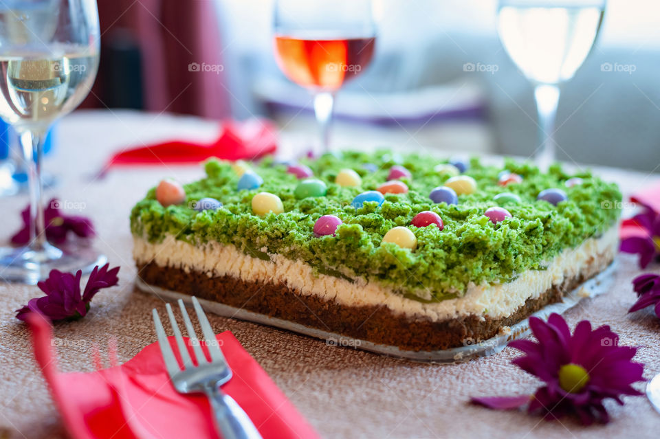 Delicious home baked cheesecake with green like grass and colorful sweets on the top served with a glass of wine.