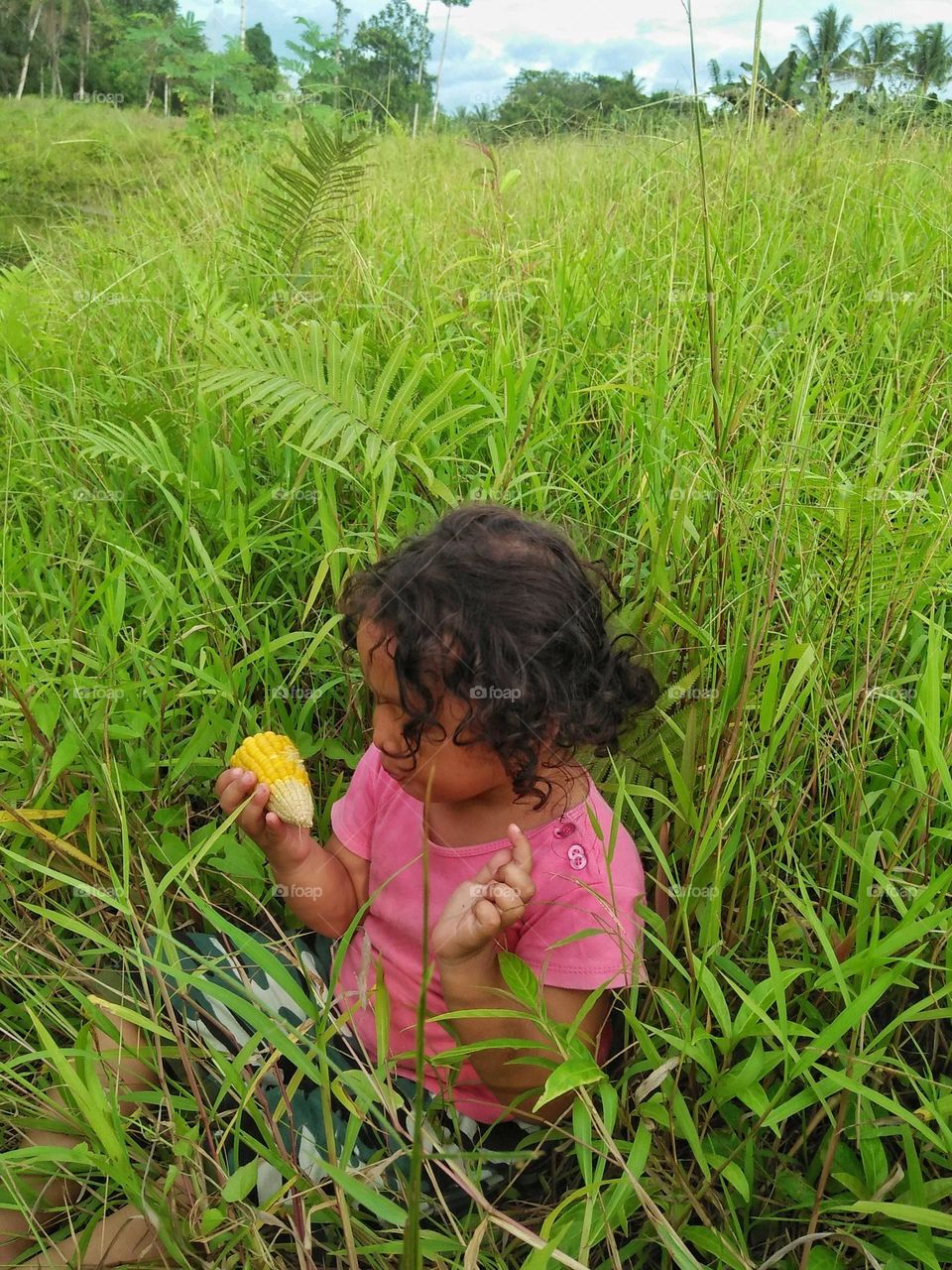 A small child is enjoying corn on the cob in a bush.