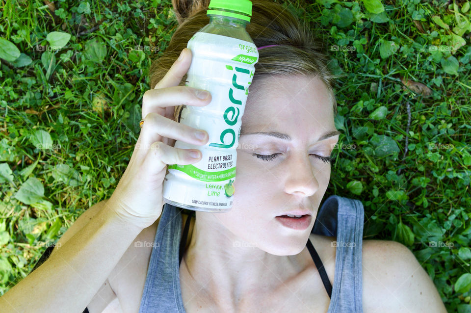 Woman laying in the grass and using a water bottle to cool her head