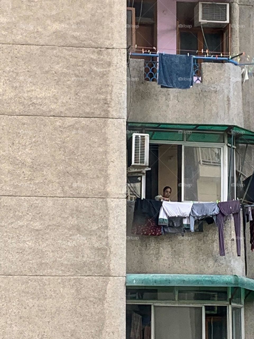 A house help hanging washed clothes for drying in the sun from the window of the balcony outside on the wire tied to the wall.