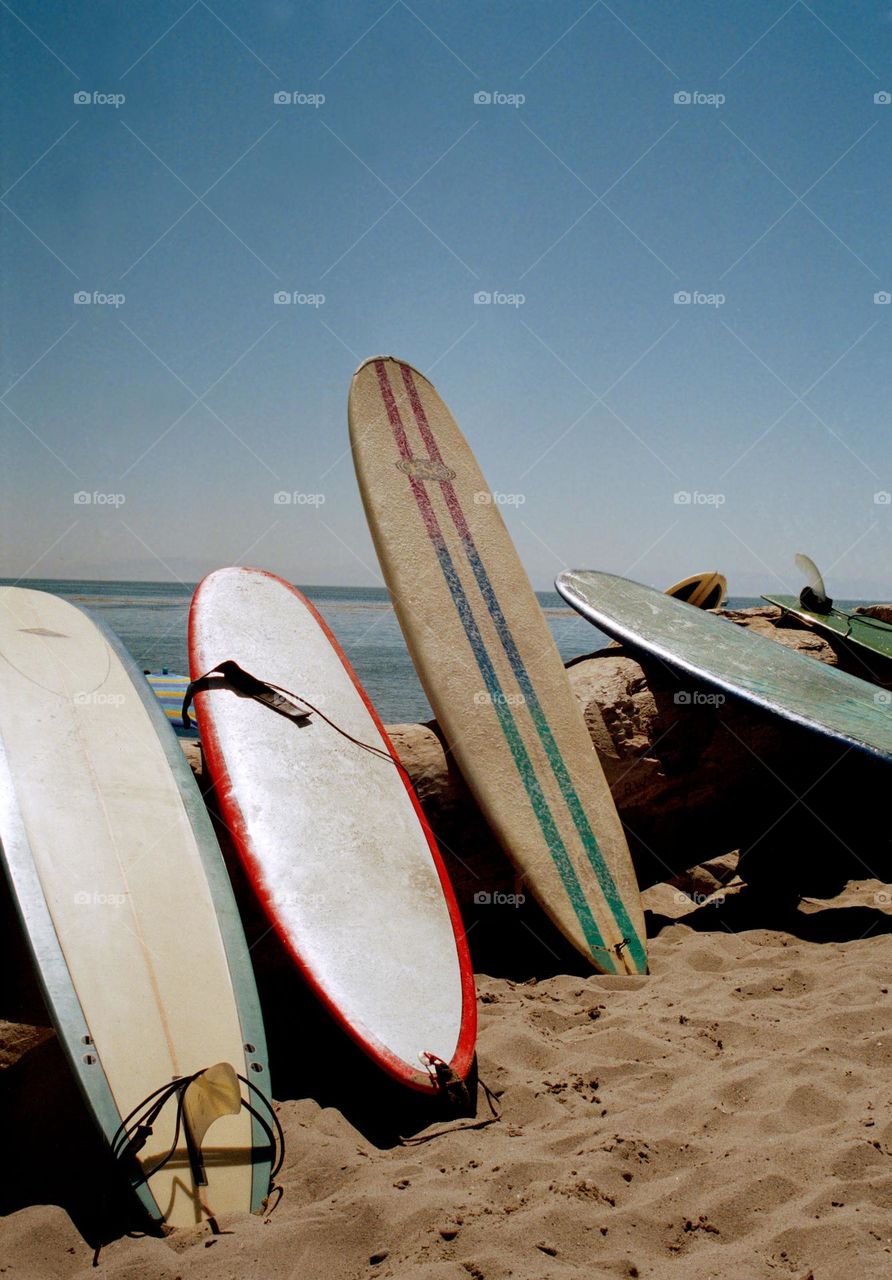 Surfboards leaning up against a giant tree stump of driftwood on the beach waiting for surfers to paddle out and ride the waves on a beautiful summer day