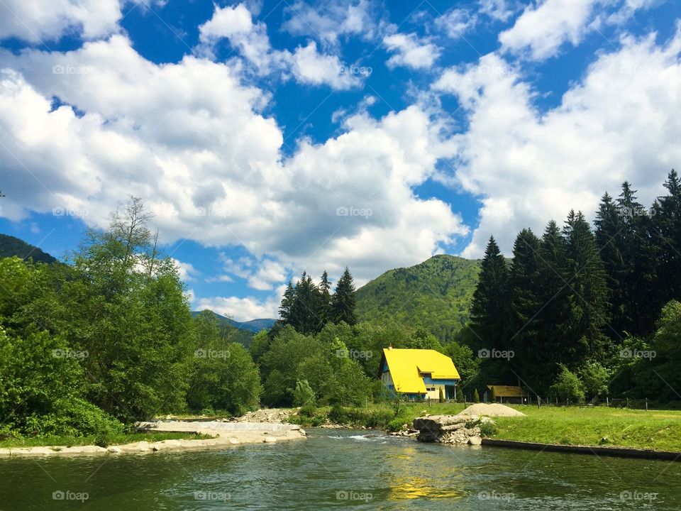 Single house surrounded by green forest and lake on a day with blue sky and clouds 