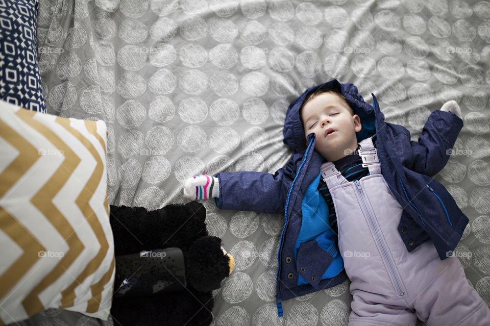 Toddler in snow suit sleeping on a bed