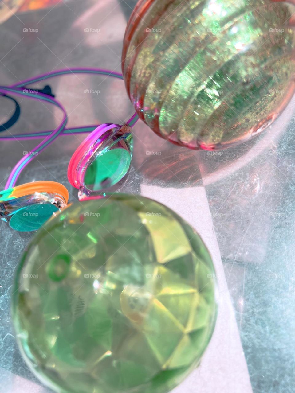 Speedo swim goggles and sparkly pool toys rest on a scratched plastic poolside table that reflects the cool blue water in the pool