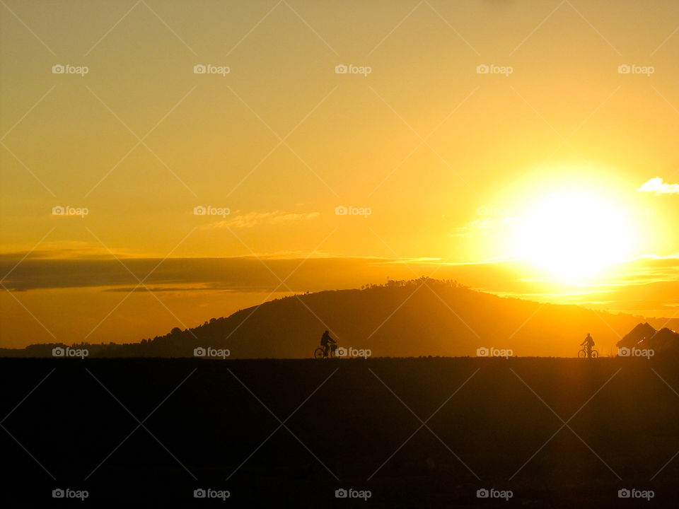People silhouetted on horizon cycling home after work with golden yellow and orange sunsets over the hill. Workers riding home on bicycle in Antananarivo Madagascar in Africa. African sunset.